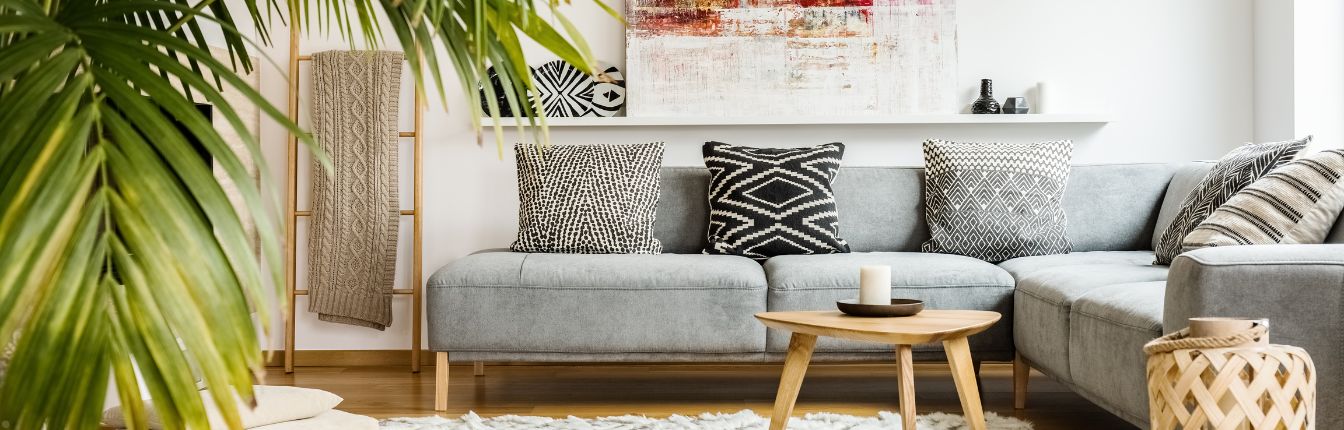 A living room with a grey couch, palm plant, and wooden table.