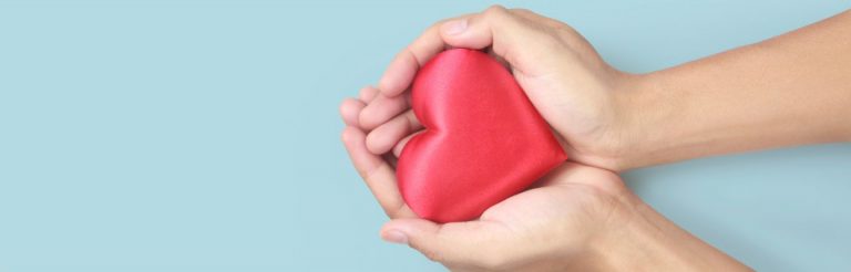 Two hands holding a red heart, against a light blue background.